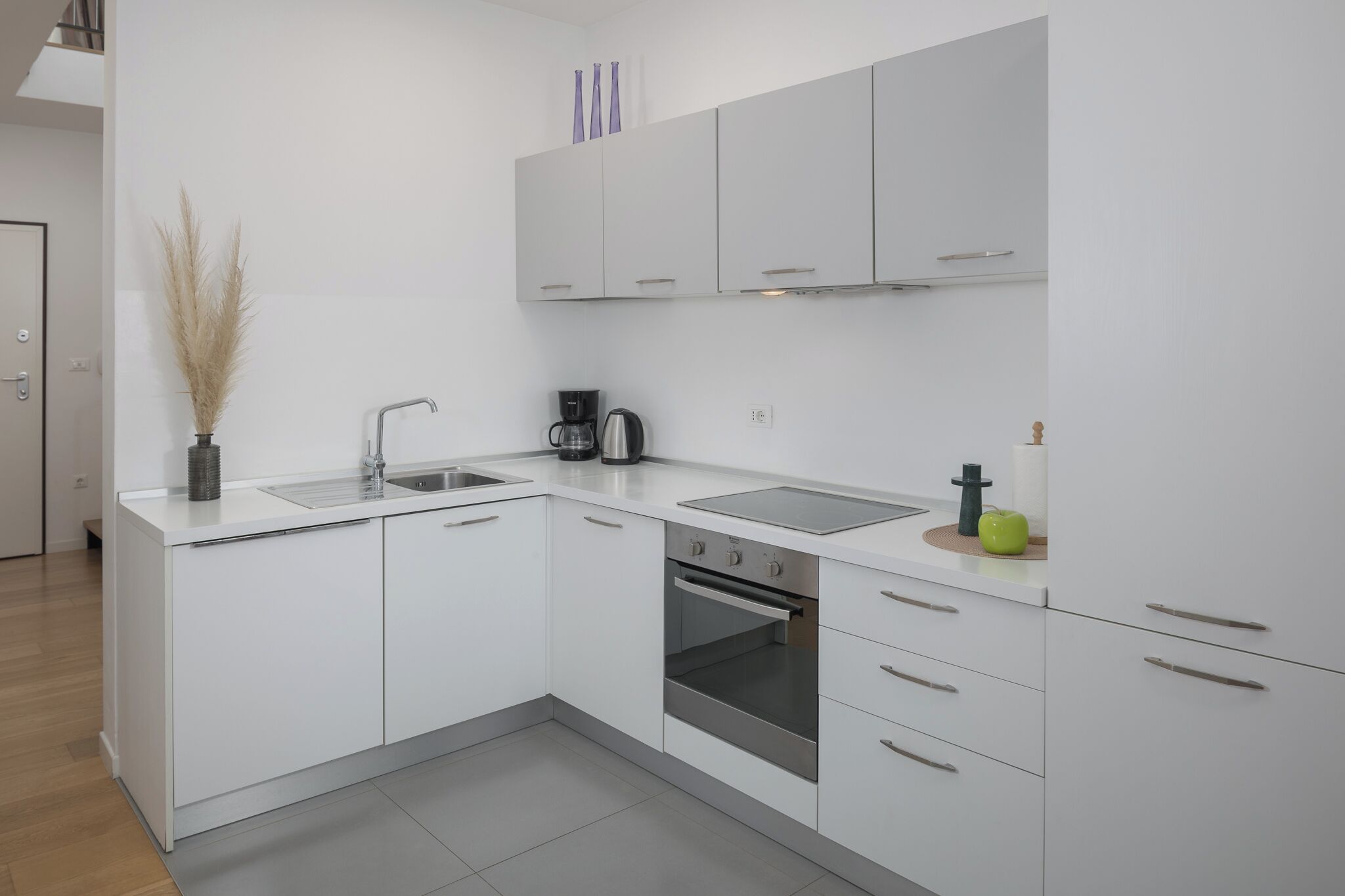 A modern kitchen with white cabinetry, a stainless steel sink, a coffee maker, and an oven.
