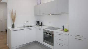 Une cuisine moderne avec des meubles blancs, un évier en acier inoxydable, une machine à café et un four.