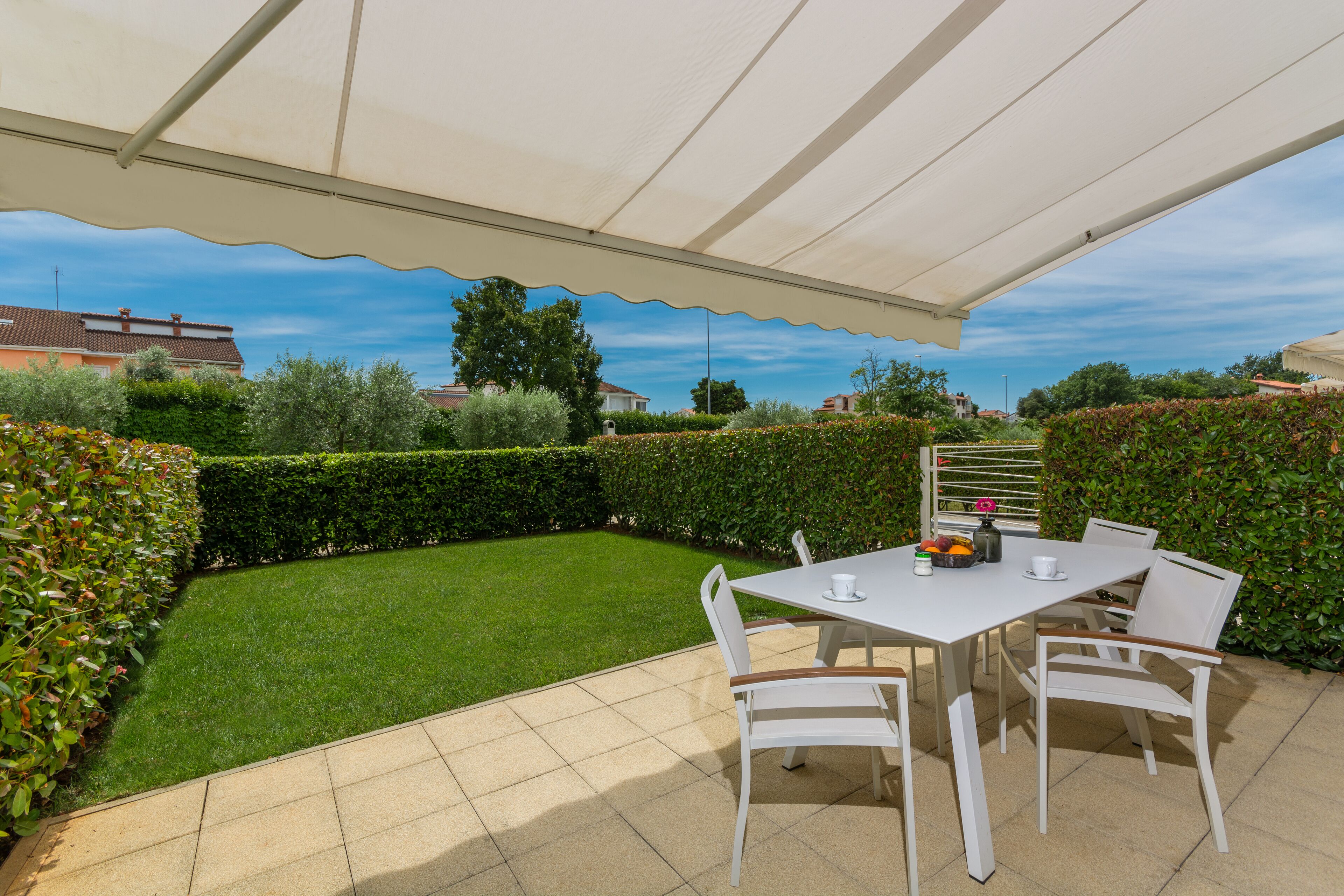 Une terrasse extérieure avec une table et des chaises, entourée d’une pelouse bien entretenue et de haies.