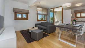 A modern living room with a grey sofa, a small round table, and a TV. There's a dining area with a wooden table and chairs. - Apartments Maj Residence Premium (Porec)