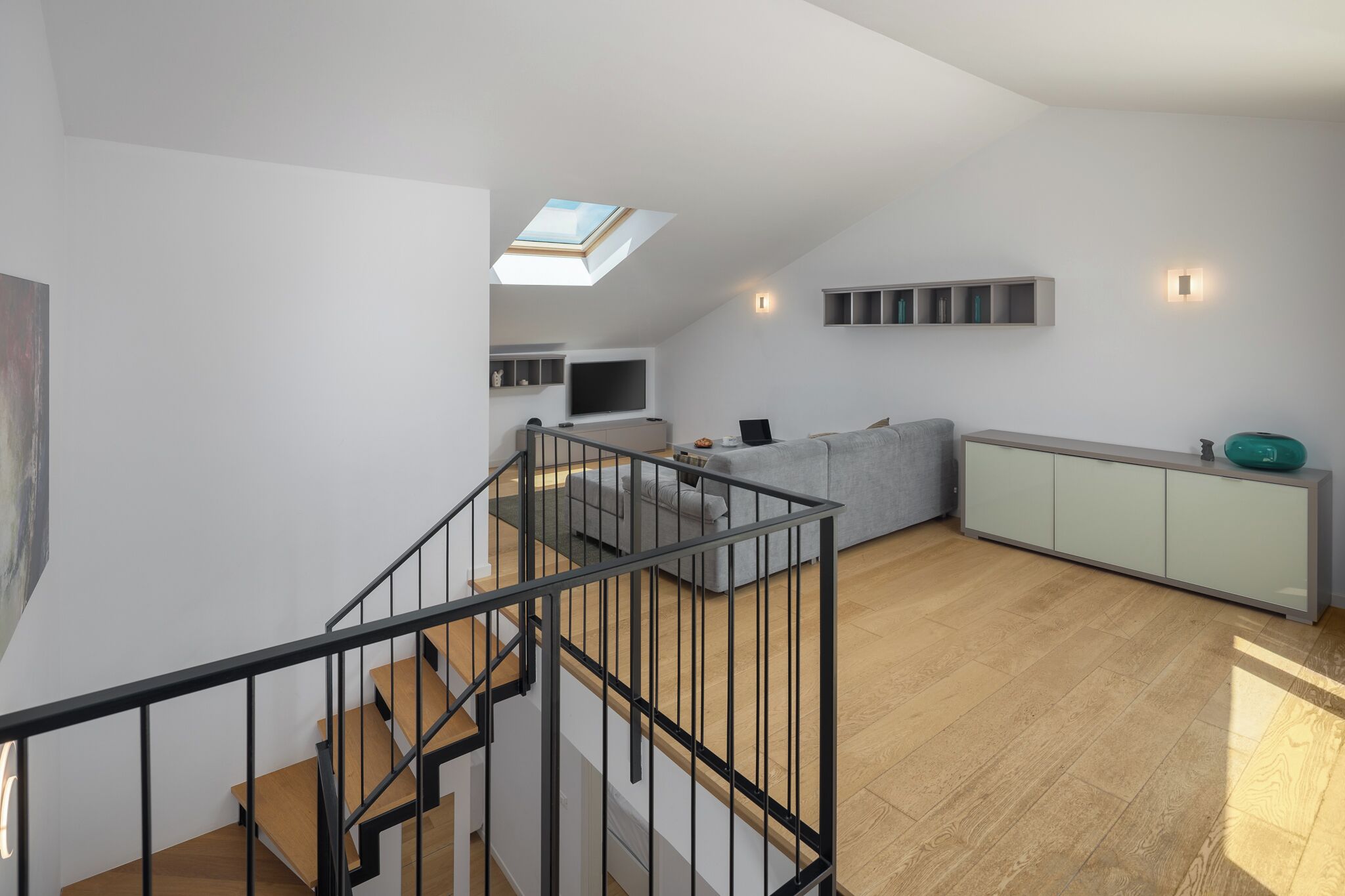 Un intérieur moderne avec un escalier, un espace de vie comprenant un canapé et un téléviseur, une lucarne et un plancher en bois de couleur claire.