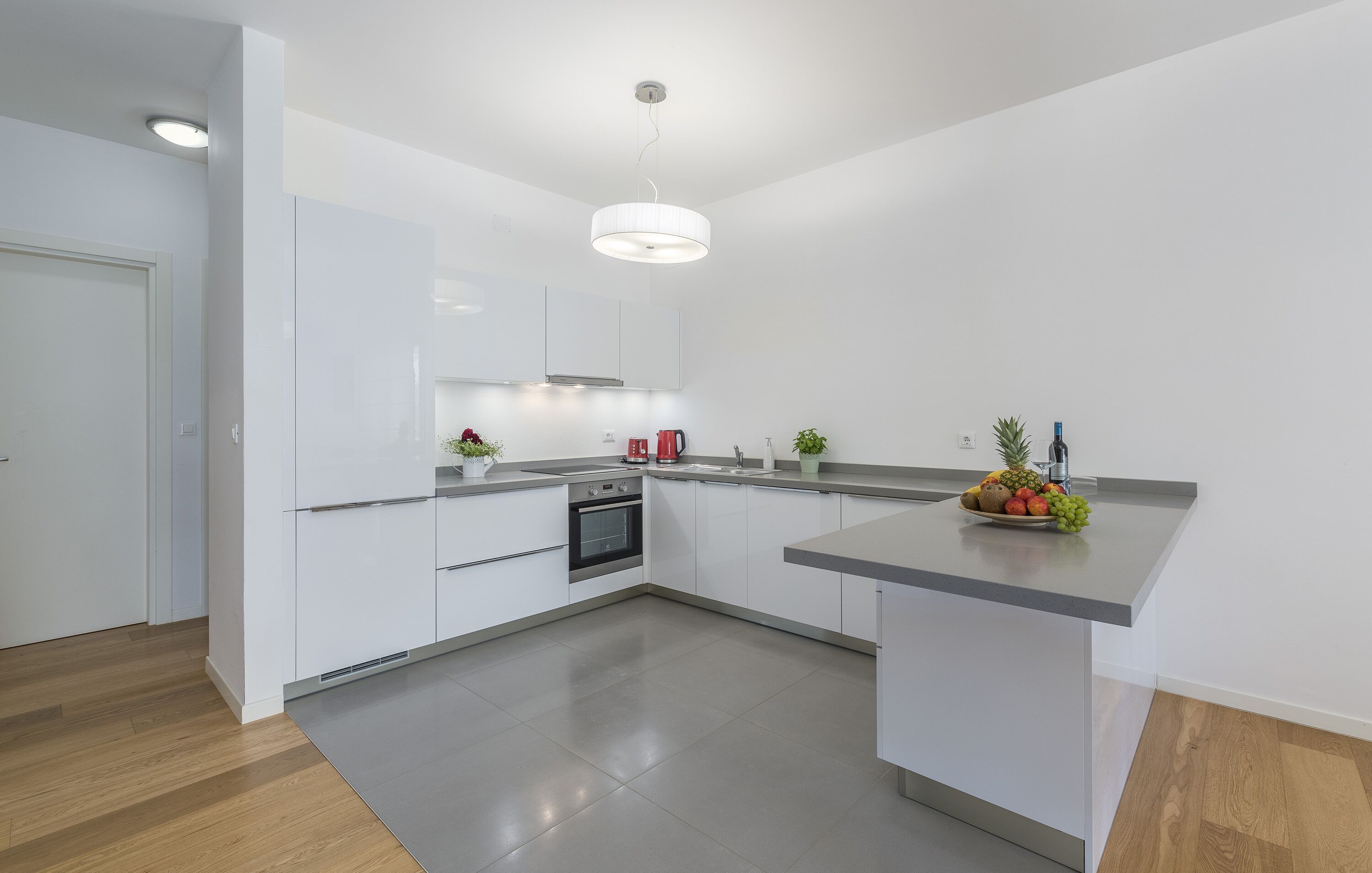 A modern kitchen with white cabinets, a stainless steel oven, and a grey countertop.