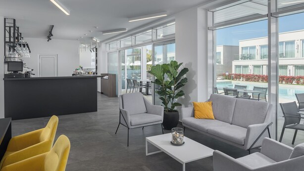 A modern hotel lobby with a bar, seating area, and a view of a pool. - Apartments Maj Residence Premium (Porec)