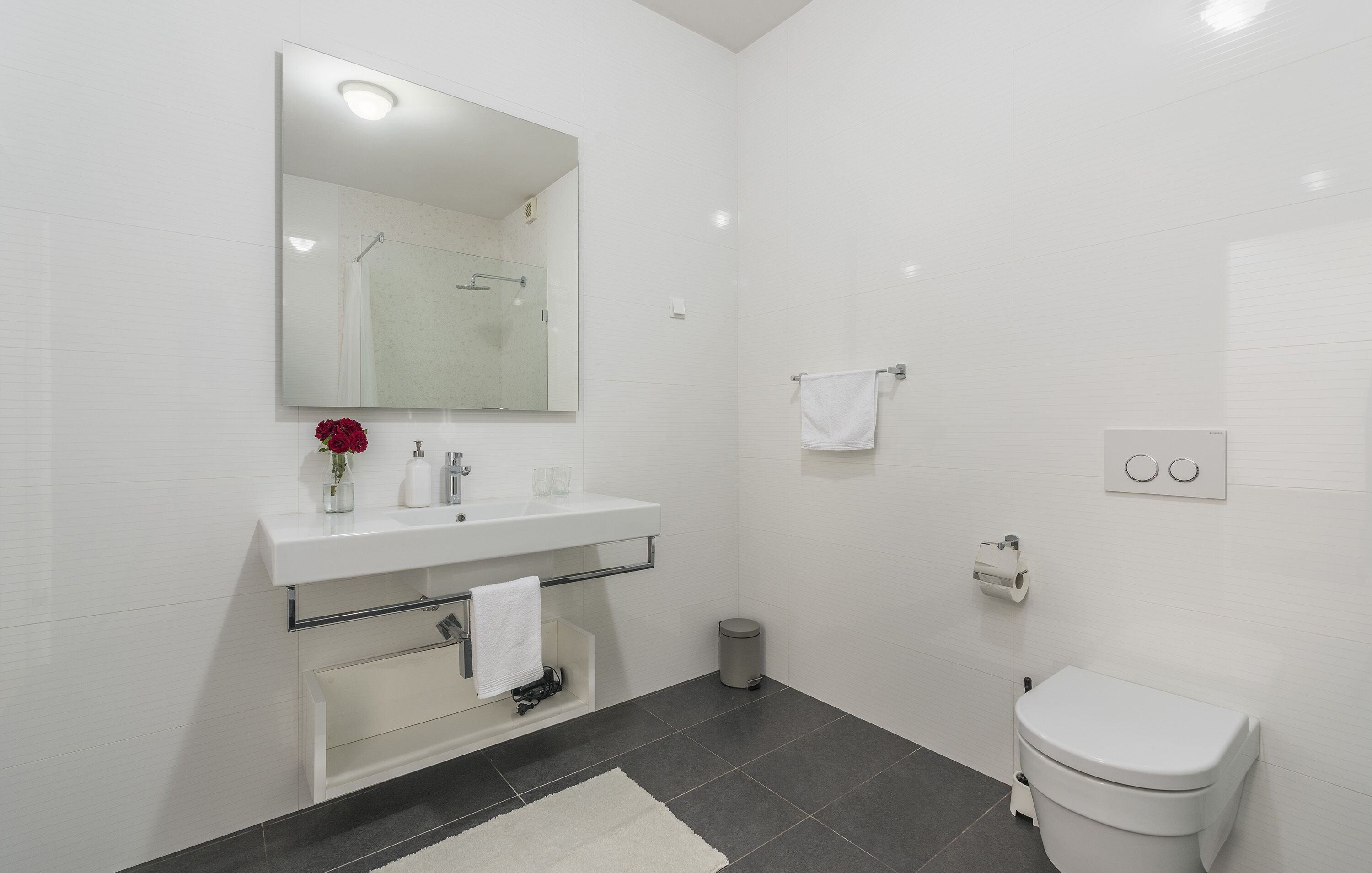 A modern bathroom with a white sink, mirror, and toilet.