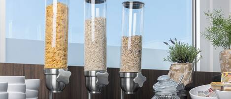 Three cylindrical dispensers filled with different grains, a white bowl, a jar, and a potted plant on a counter.