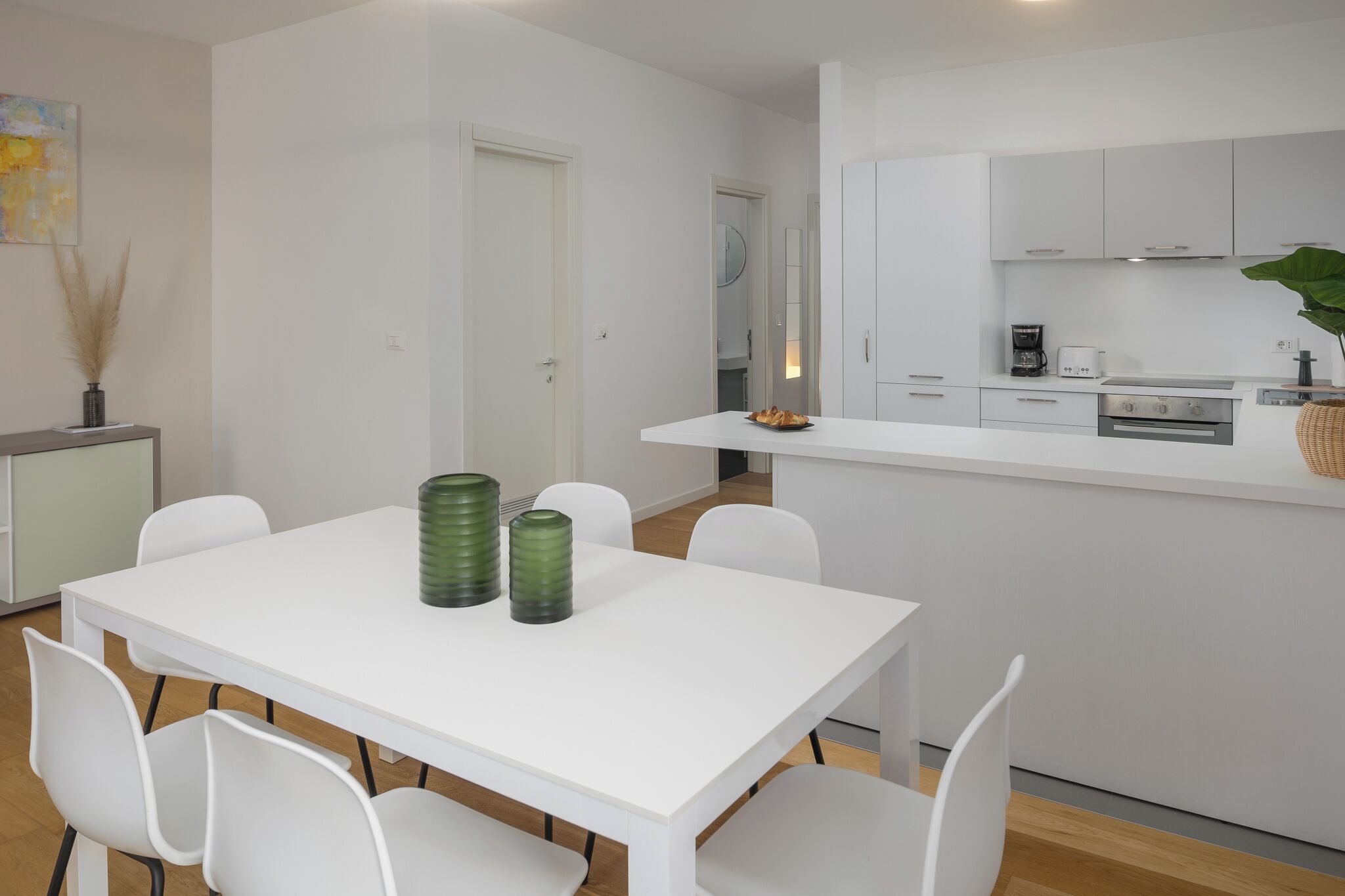 Una cucina moderna con mobili bianchi, un'isola centrale e un'area da pranzo con tavolo e sedie bianche.