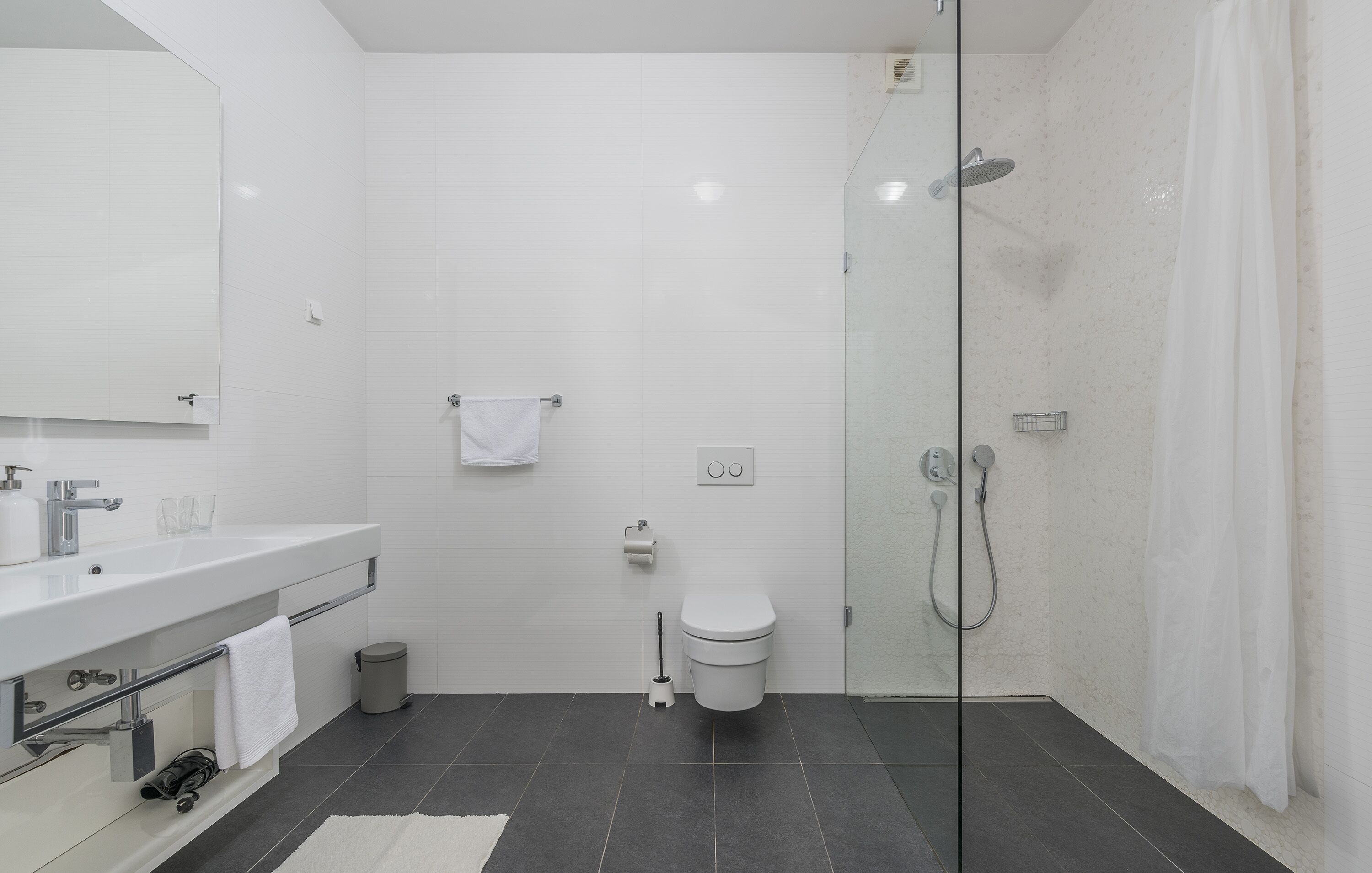 Un baño moderno con ducha envuelta en vidrio, un lavamanos blanco y un inodoro.