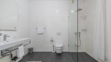 Un baño moderno con ducha envuelta en vidrio, un lavamanos blanco y un inodoro.