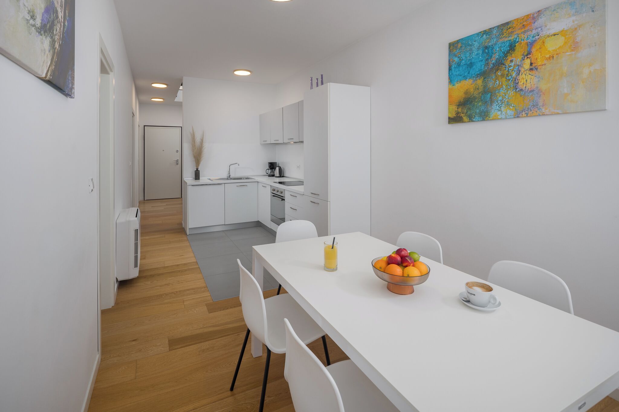 A modern kitchen with white cabinets, a dining table with chairs, and a fruit bowl.