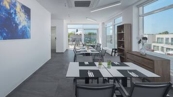 A modern dining area with tables set for meals, large windows, and a view of buildings.