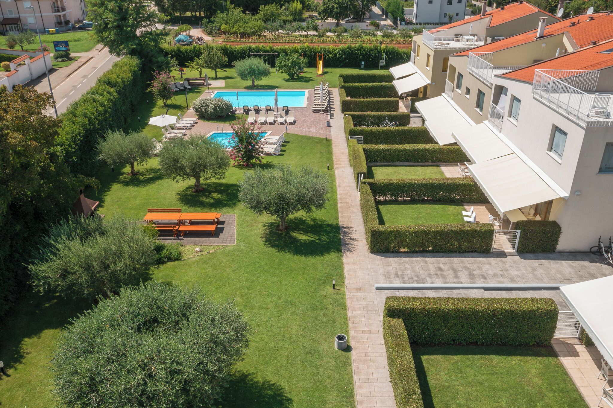 A residential area with a swimming pool, lounge chairs, and neatly trimmed hedges.