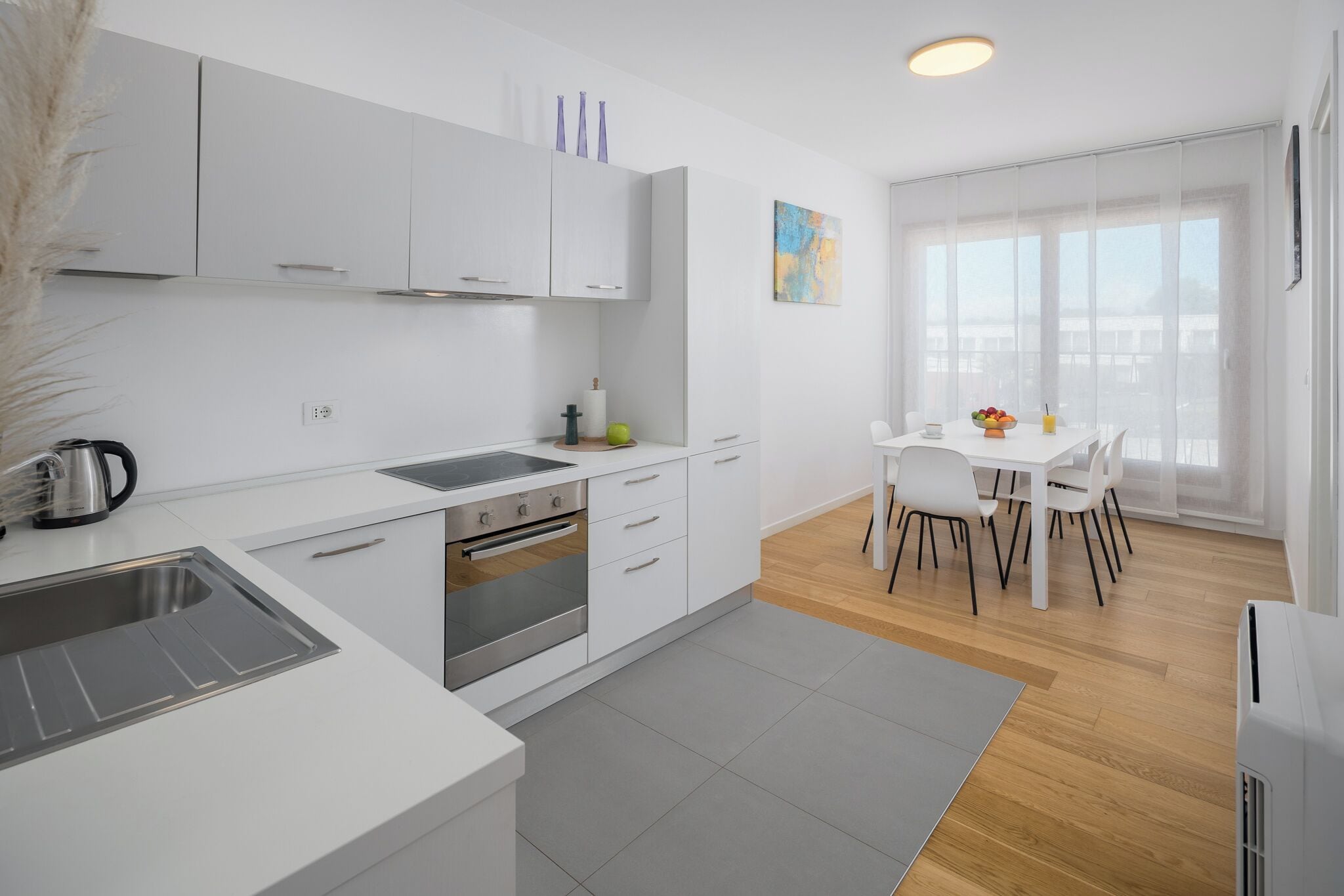 A modern kitchen with white cabinets, a built-in oven, and a dining area with a white table and chairs.