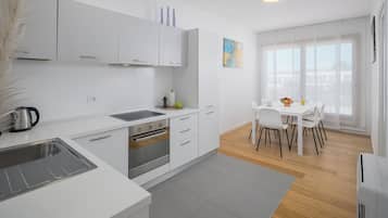 A modern kitchen with white cabinets, a built-in oven, and a dining area with a white table and chairs.