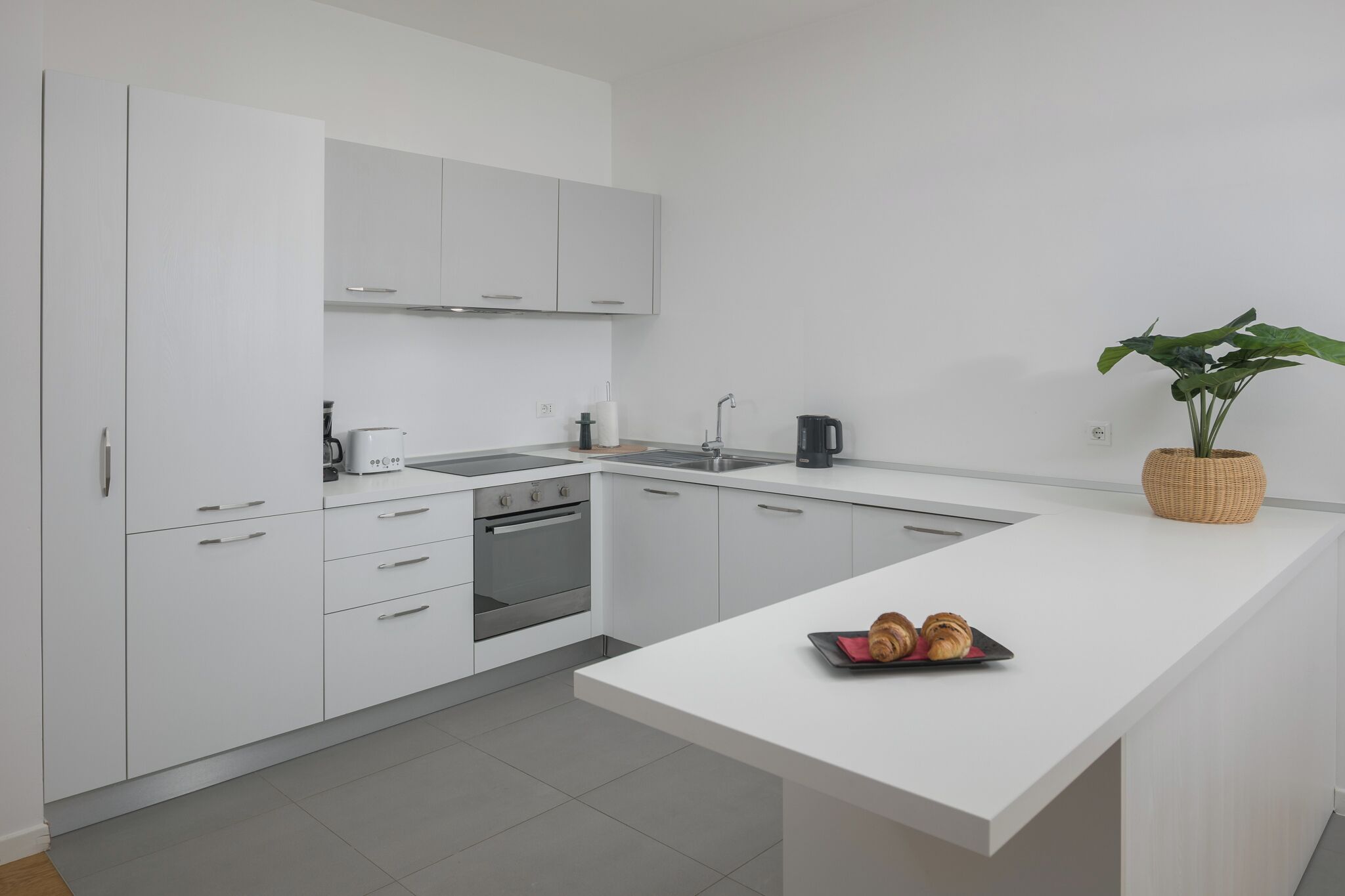 A modern kitchen with white cabinetry, a built-in oven, a sink, and a small island with croissants.