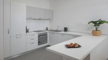A modern kitchen with white cabinetry, a built-in oven, a sink, and a small island with croissants.