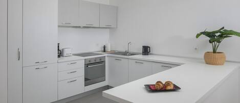 A modern kitchen with white cabinetry, a built-in oven, a sink, and a small island with croissants.