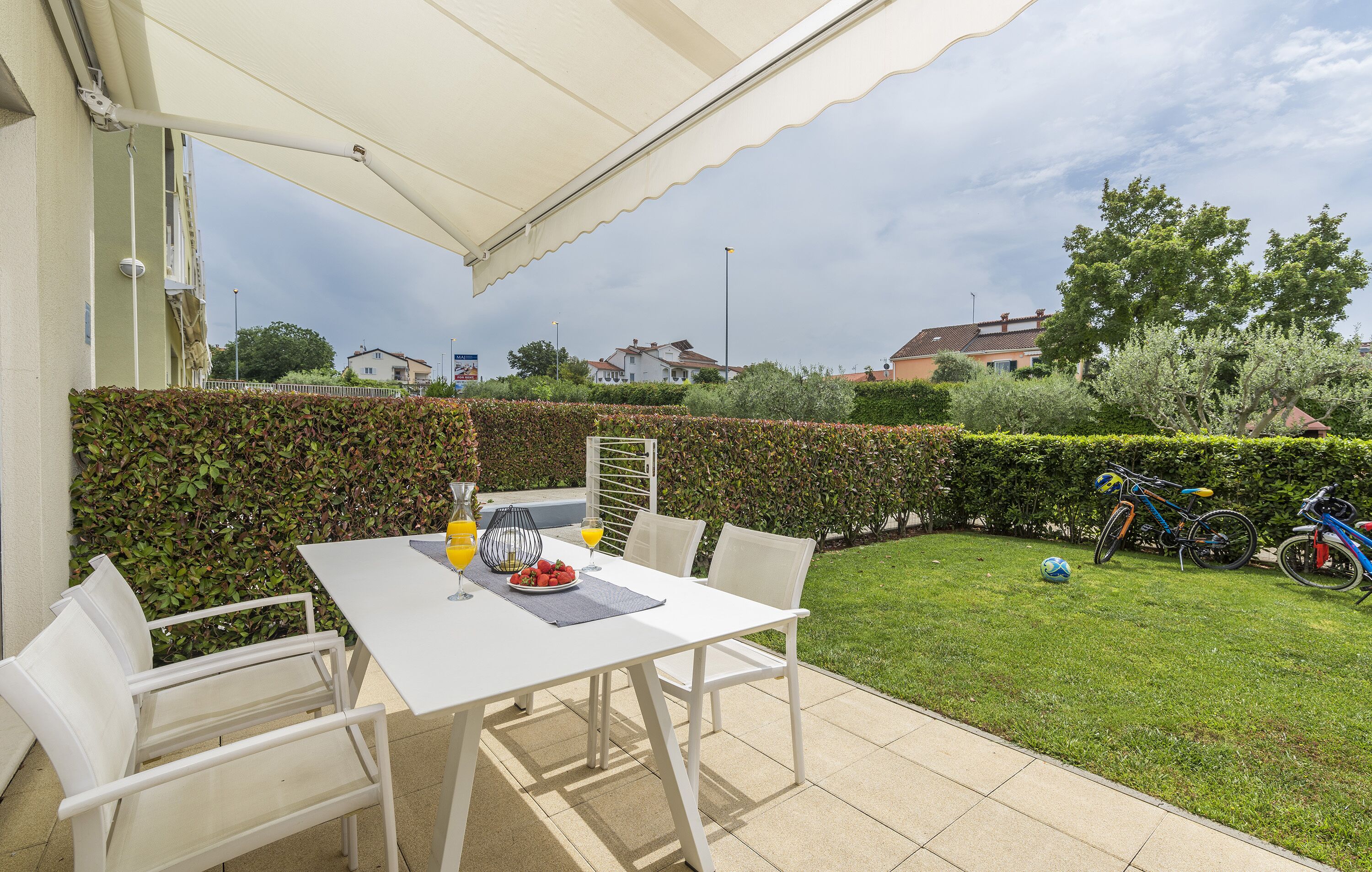 A patio with a white table and chairs, a table umbrella, and a bicycle in the background.