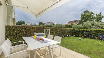 A patio with a white table and chairs, a table umbrella, and a bicycle in the background.