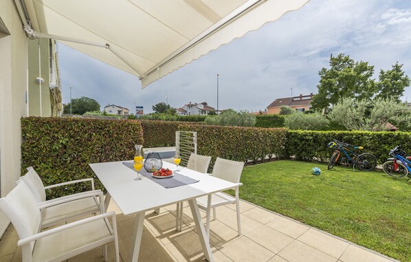 Une terrasse avec une table et des chaises blanches, un parasol et un vélo en arrière-plan.