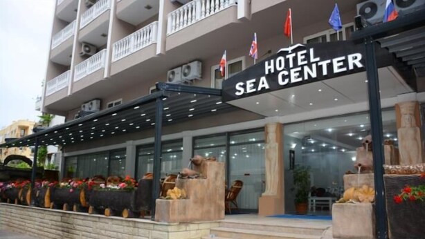 Et hotel kaldet "Hotel Sea Center" med en moderne facade, udendørs siddeområde og dekorative plantekasser.