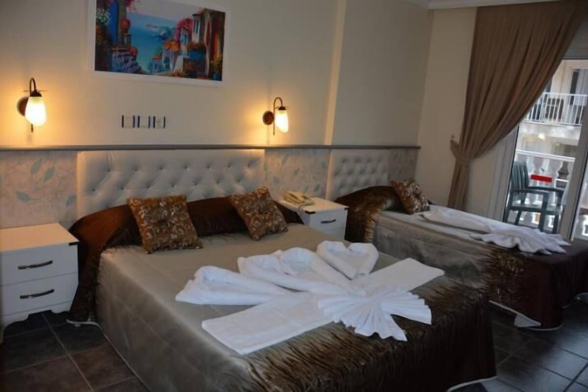 A hotel room with a large bed, two bedside tables, a painting on the wall, and a view of the outside balcony.