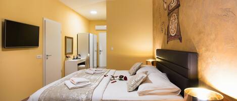 A hotel room with a bed, bedside tables, a TV, a mirror, and a wall clock.