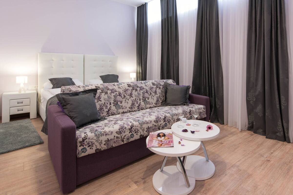 Un dormitorio moderno con un sofá púrpura, una mesa redonda blanca y una mesita de noche con una lámpara.