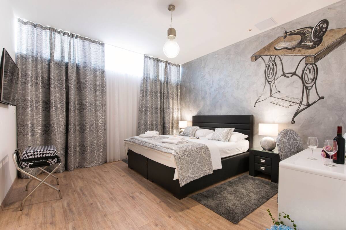 Un dormitorio moderno con una cama grande, un aparador, una silla, una lámpara y un cuadro en la pared.