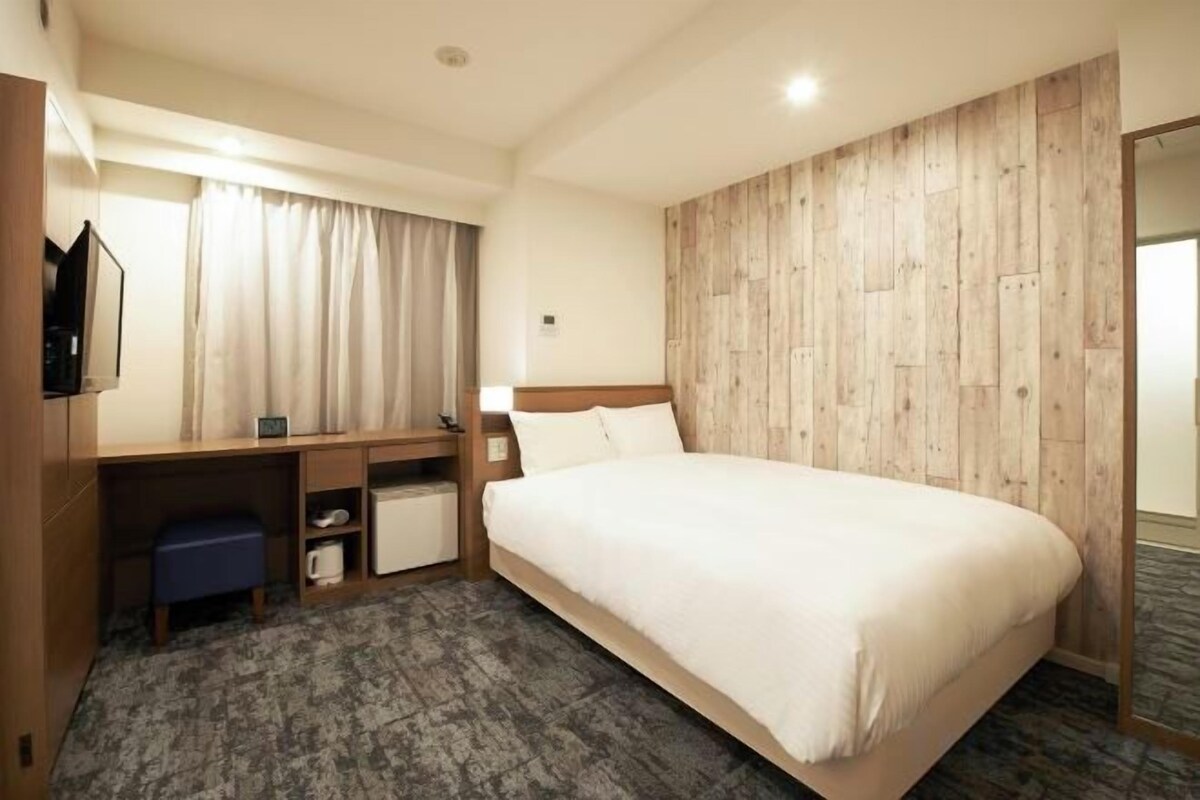 Una habitación de hotel con una cama, un escritorio con una silla, un televisor y un armario.