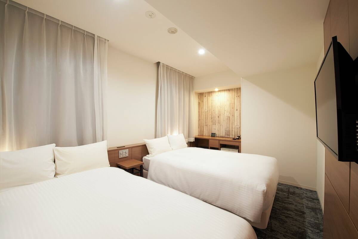 A hotel room with two beds, a desk, a chair, a TV, and a wooden panel wall.