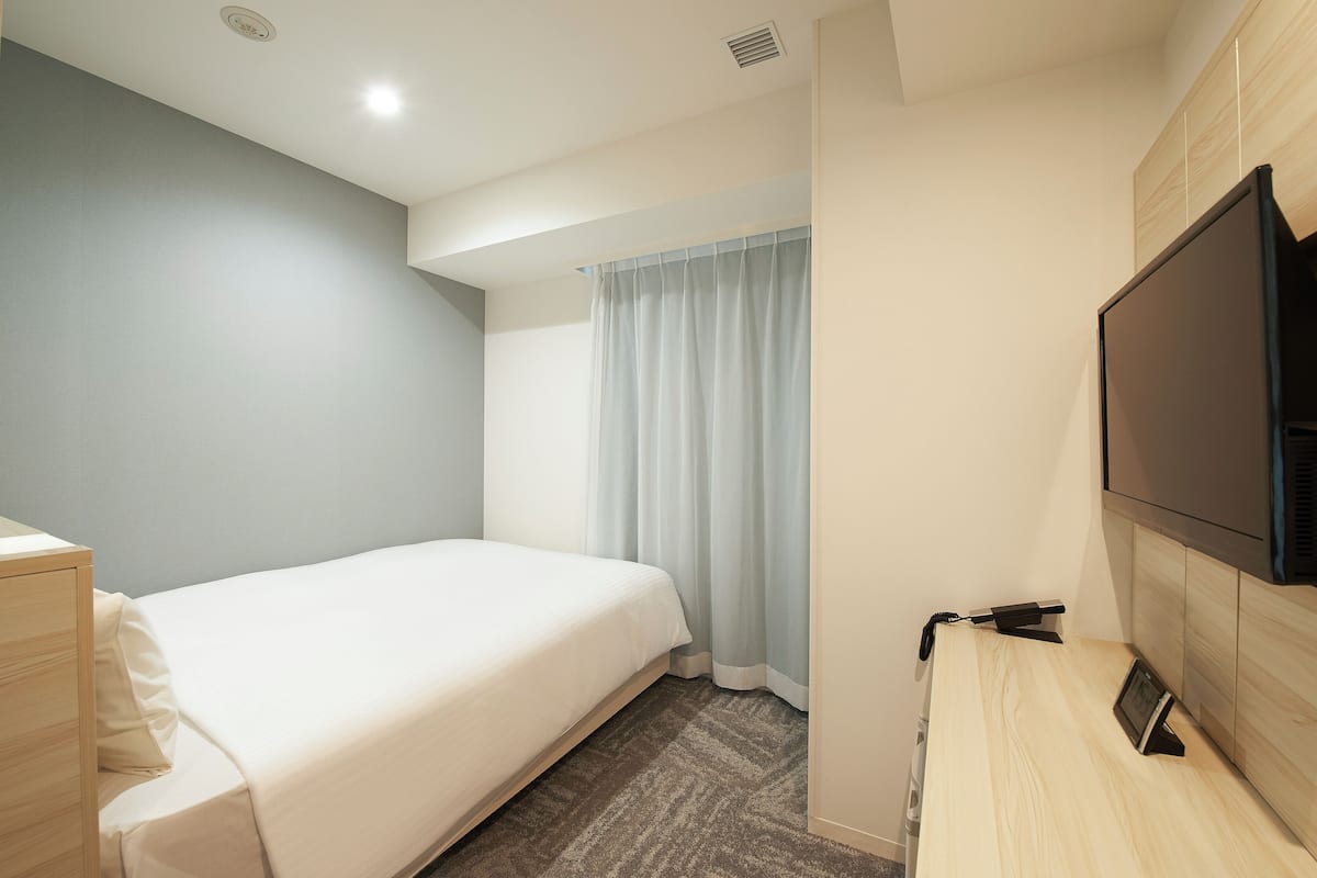A hotel room with a bed, a desk, a television, and a window with curtains.