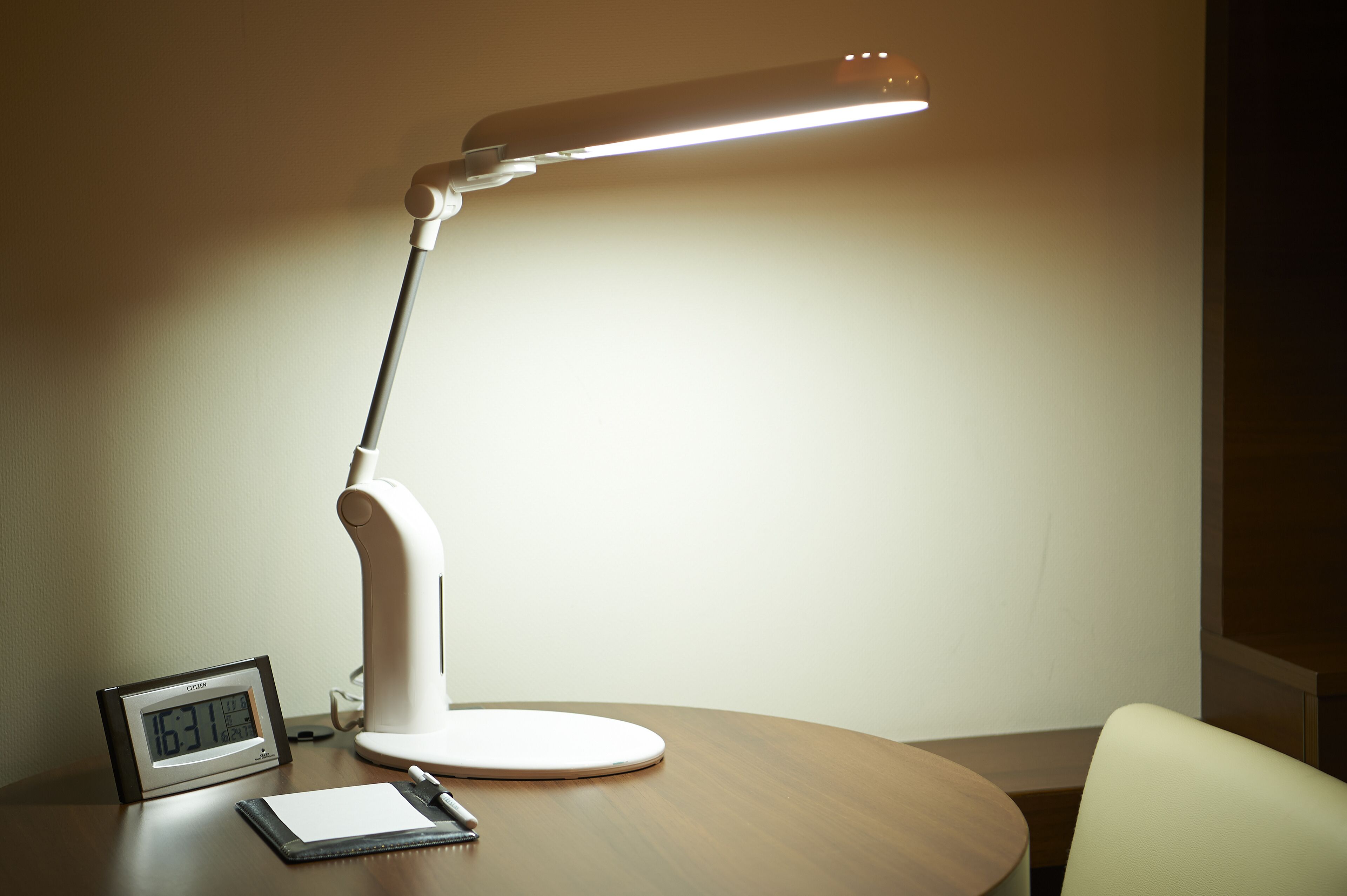 A desk with a white desk lamp, a digital clock, and a notepad.