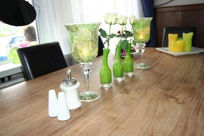 Una mesa de comedor con vasos de vidrio verde, saleros blancos y velas.