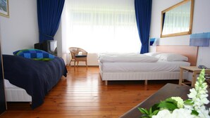 Ein Hotelzimmer mit zwei Betten, Holzboden, Fernseher, einem Sessel und einem Tisch mit Blumen.