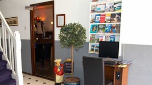 Ein Empfangsbereich mit einer Rezeption, einem Computermonitor, einem kleinen Topfpflanzen und einer Statue.