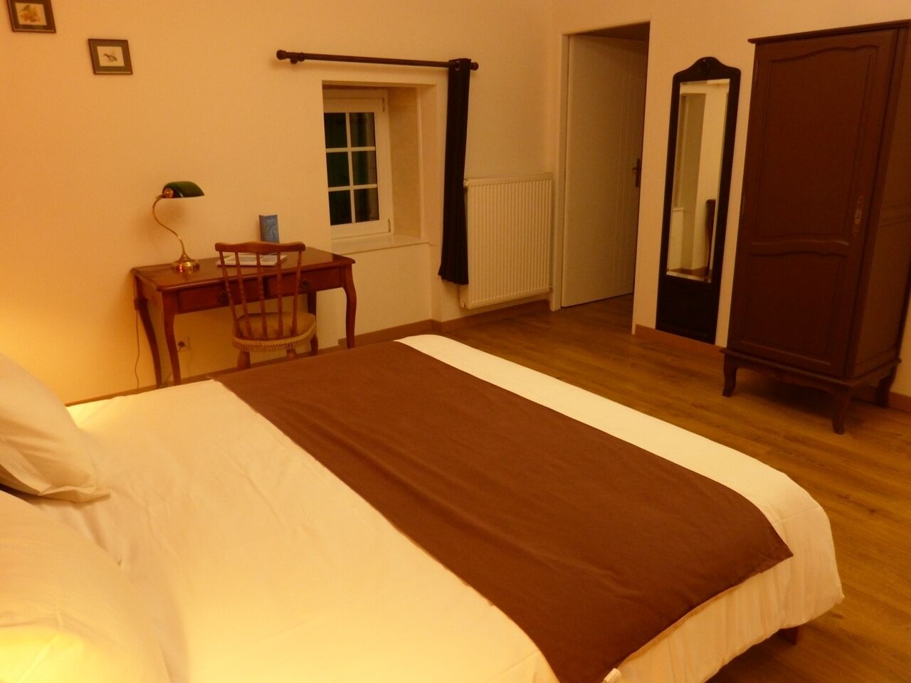 A bedroom with a bed, a desk, a chair, a window, a radiator, a wardrobe, and a mirror.