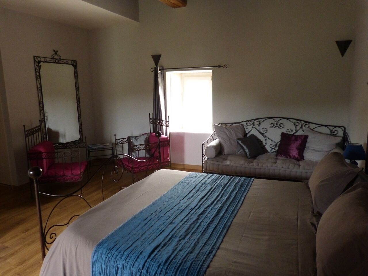 A bedroom with a large bed, a sitting area with a sofa and armchairs, a mirror, and a window with curtains.