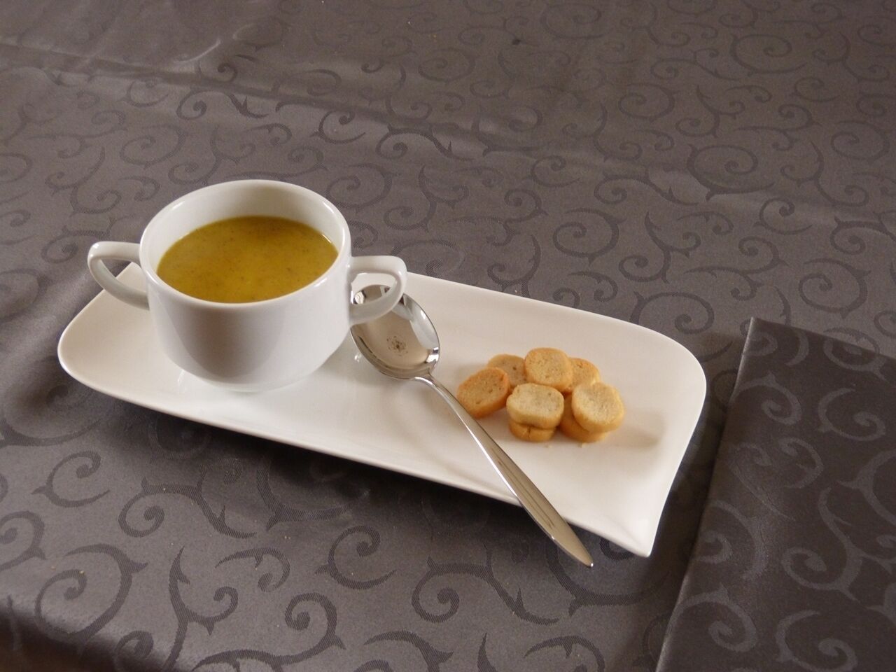 Una taza blanca de sopa sobre un platillo blanco, junto a un plato con varios bizcochos redondos.