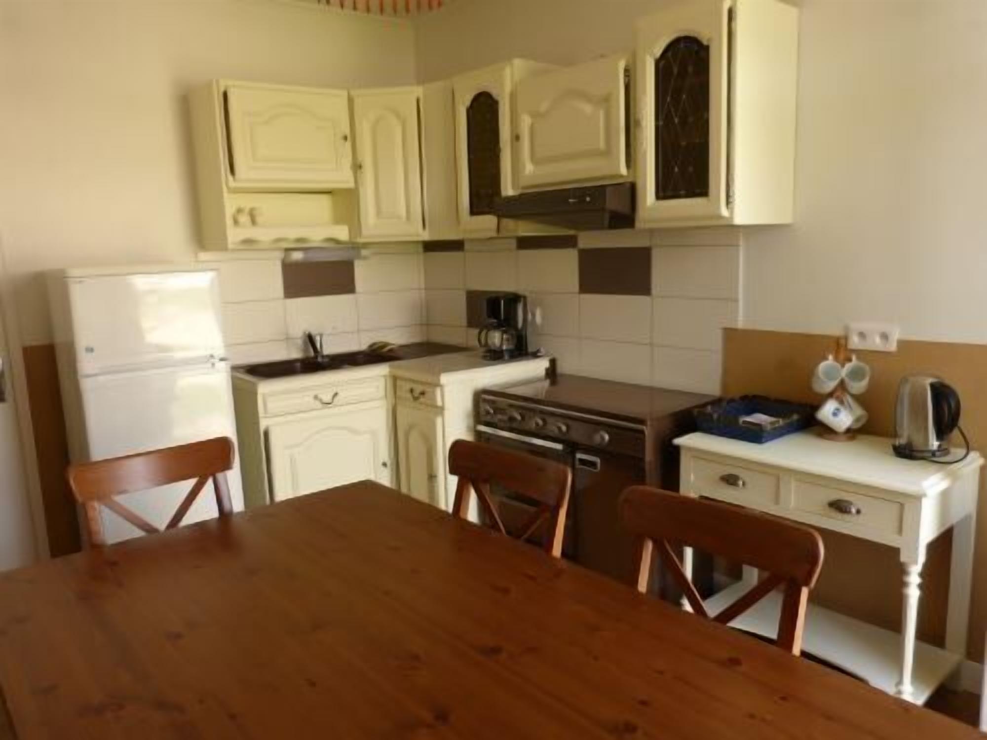 Cocina compacta con armarios blancos, estufa, lavabo y una mesa de comedor con sillas.