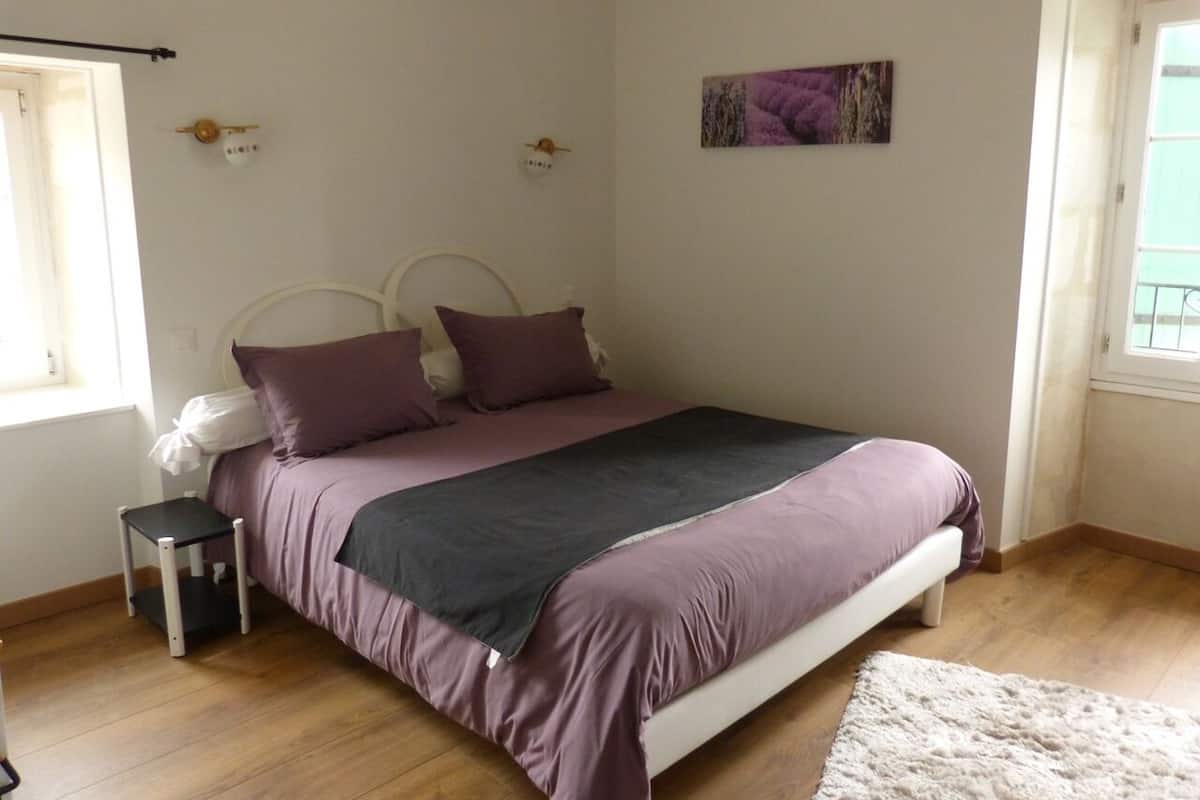 A bedroom with a bed, a small bedside table, a window, and a door.