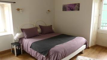 A bedroom with a bed, a small bedside table, a window, and a door.