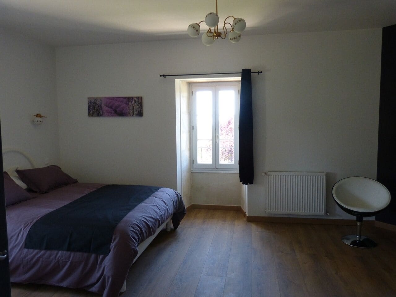 A bedroom with a bed, a radiator, a window with curtains, and a chair.