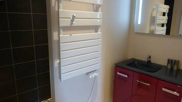 Een badkamer met een witte handdoekhouder, een wastafel met spiegel erboven en rode kastjes.