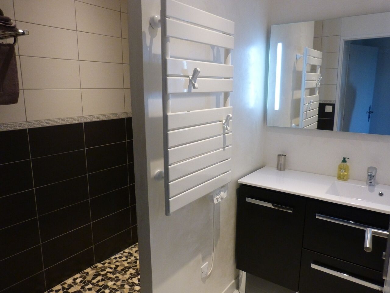Un baño con un lavamanos blanco, armarios negros, un espejo y un perchero.