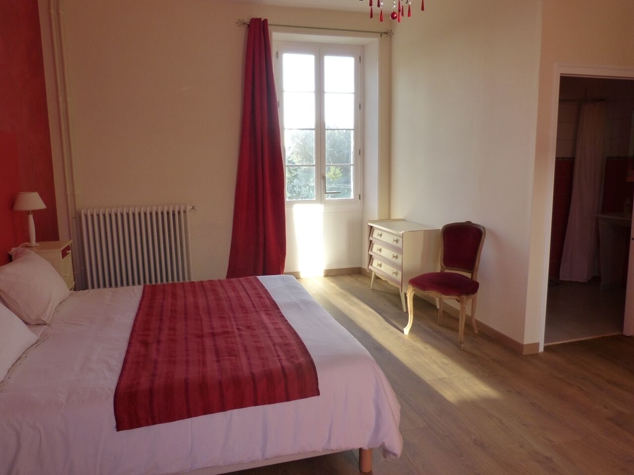 Une chambre à coucher avec un lit, une commode, une chaise et une fenêtre avec des rideaux.