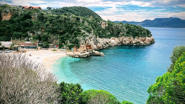 A coastal area with a beach, rocky shoreline, and a building with a red roof. - Kaktus Beach Apart (Kas)