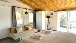 A room with a wooden ceiling, a sofa with cushions, a bed with towels, a floor lamp, and a view of the outdoors through a glass door. - Kaktus Beach Apart (Kas)