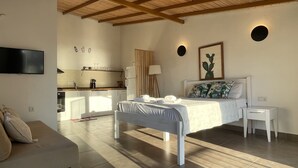 A modern bedroom with a bed, bedside tables, a TV, and a kitchen area in the background. - Kaktus Beach Apart (Kas)