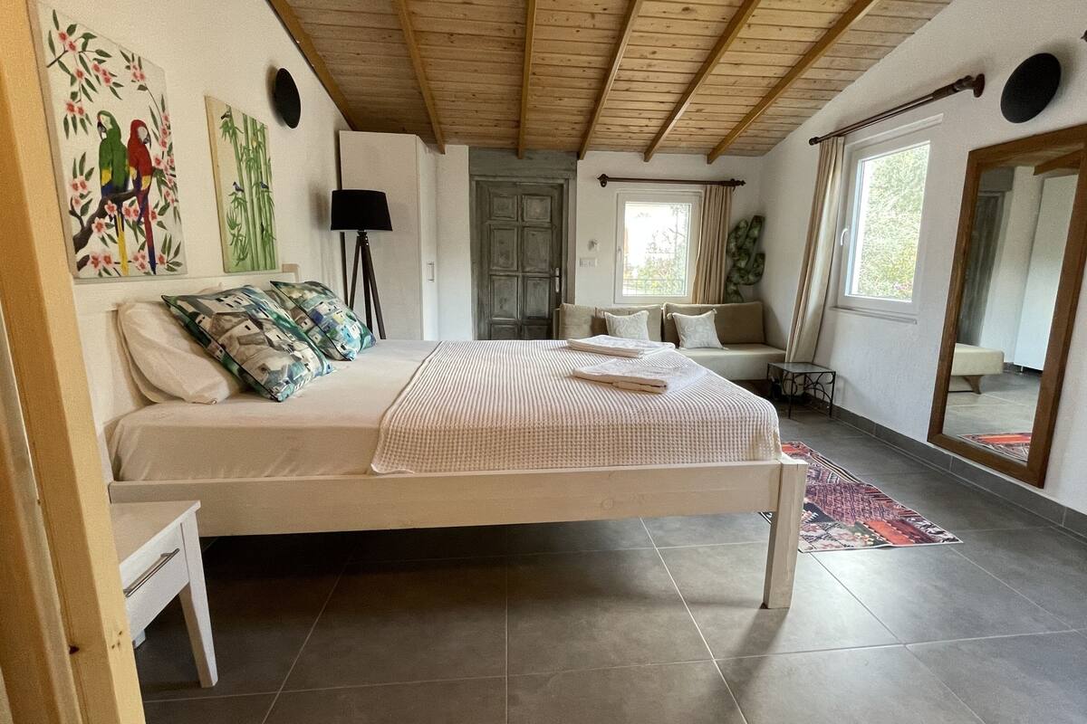 A bedroom with a bed, a sofa, a mirror, and artwork on the walls.