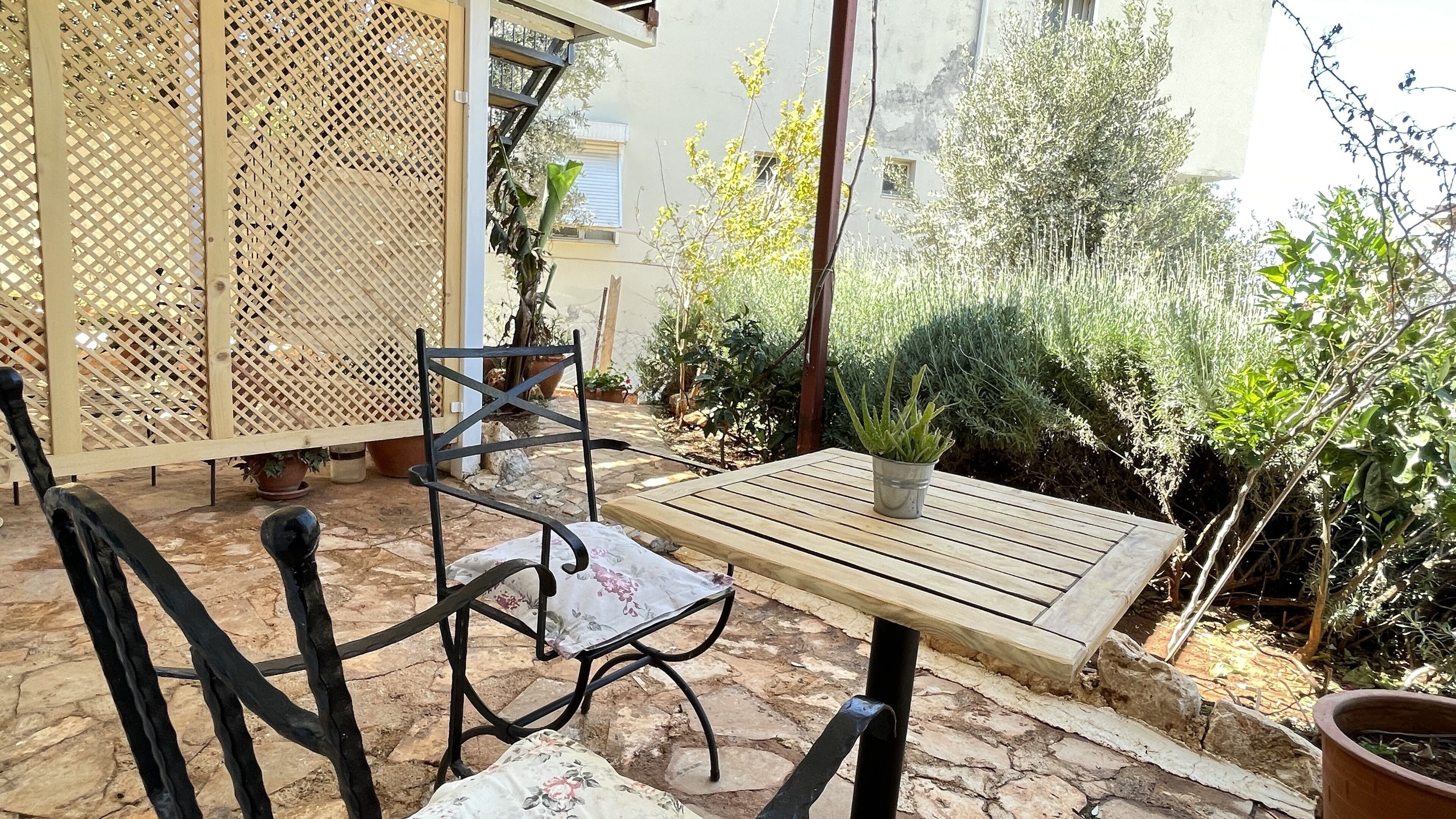 An outdoor patio with a wooden table and chairs, surrounded by potted plants and a wooden lattice fence.